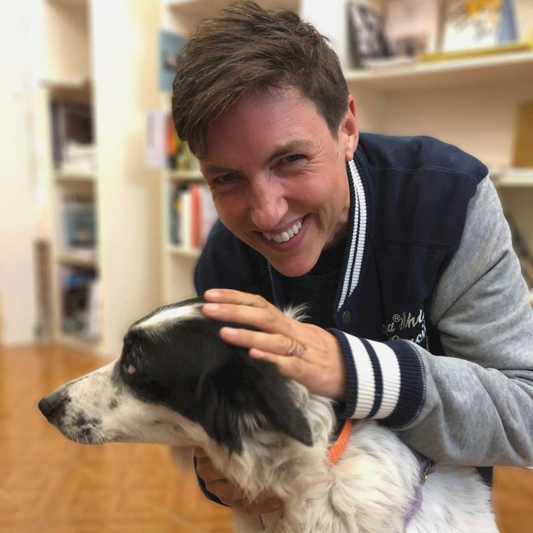 MJ smiling and stroking a black and white dog.